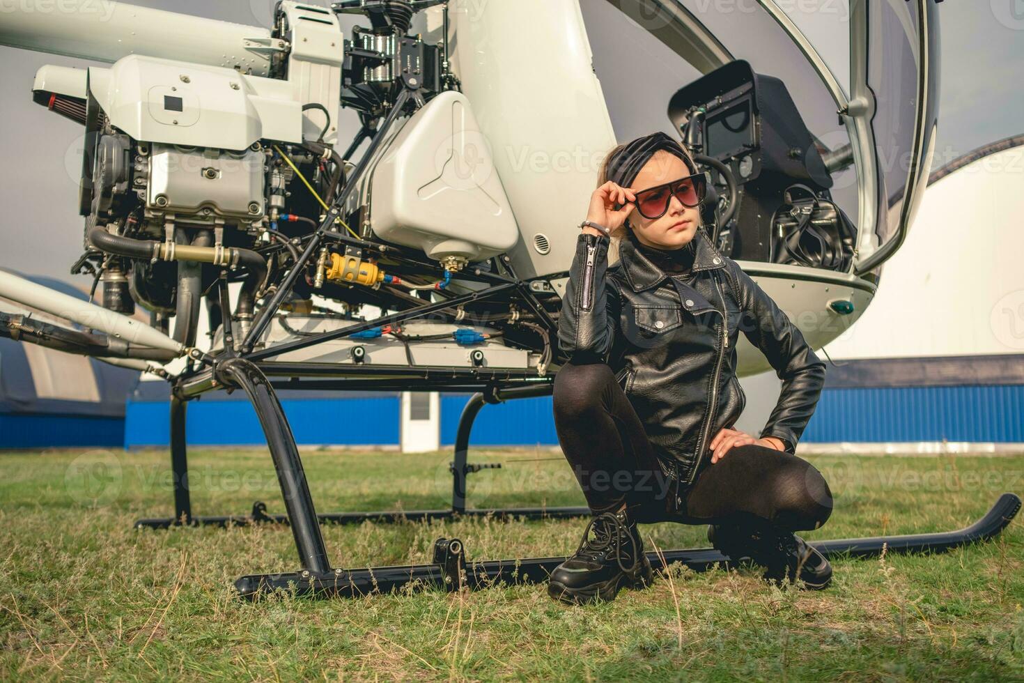 Preteen girl sitting near small helicopter at airfield photo