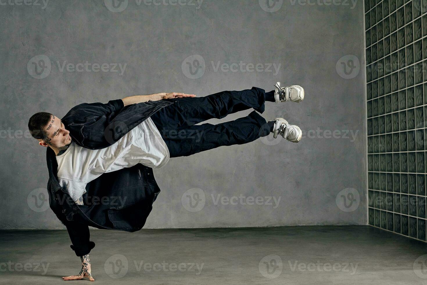 chico con tatuado cuerpo, barba. vestido en blanco camiseta y zapatillas, negro camisa, pantalones. demostración trucos en gris antecedentes. Baile (salón, hip hop foto