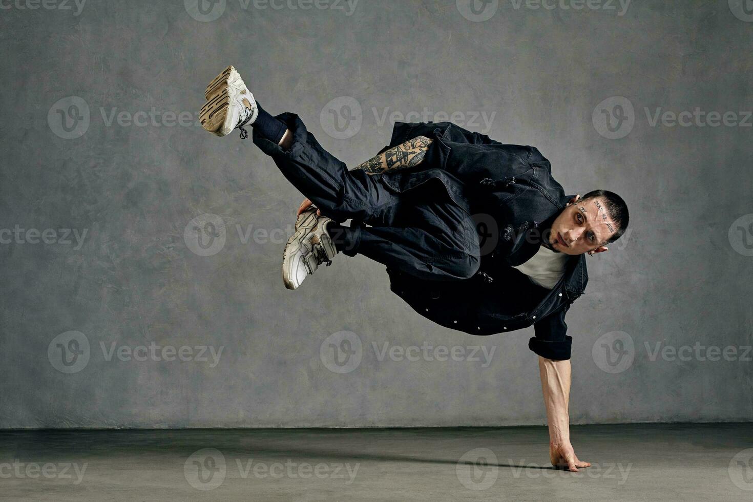 Active man with tattooed body, beard. Dressed in white t-shirt and sneakers, black shirt, pants. Dancing on gray background. Dancehall, hip-hop photo