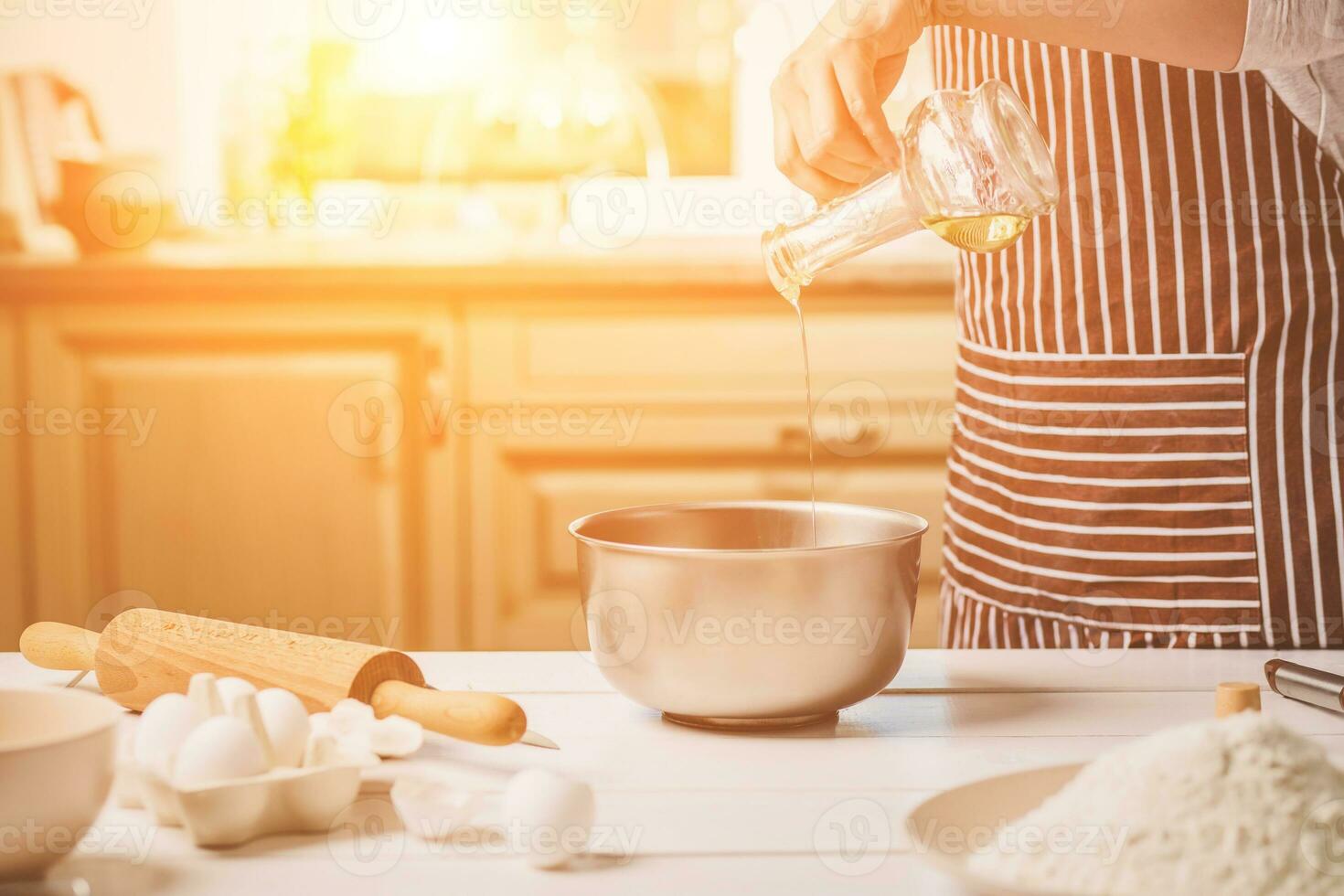 Young woman pouring oil into a bowl with dough, close-up photo