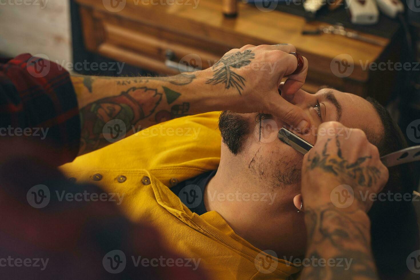 Client during beard shaving in barber shop photo