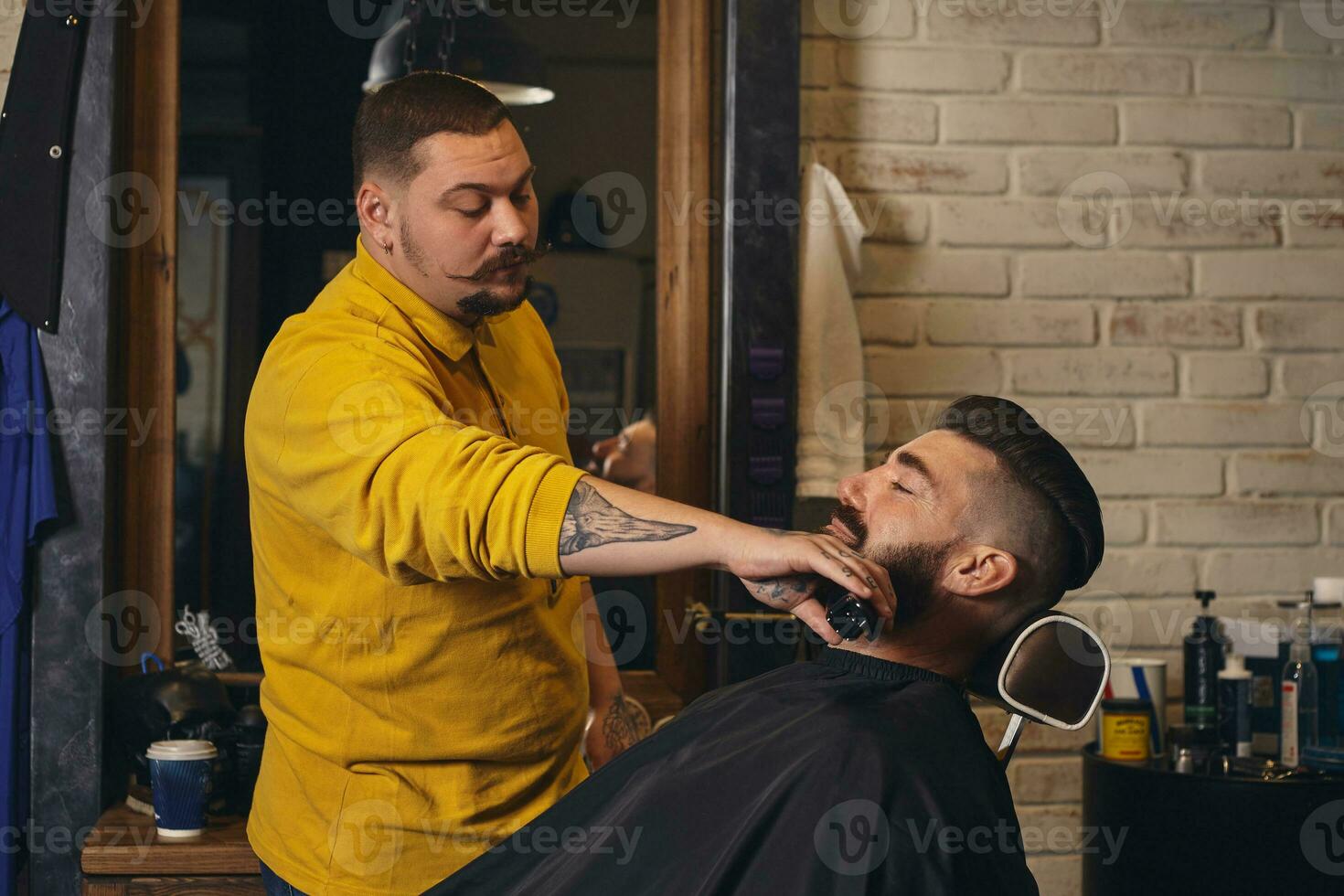 Client with big black beard during beard shaving in barber shop photo