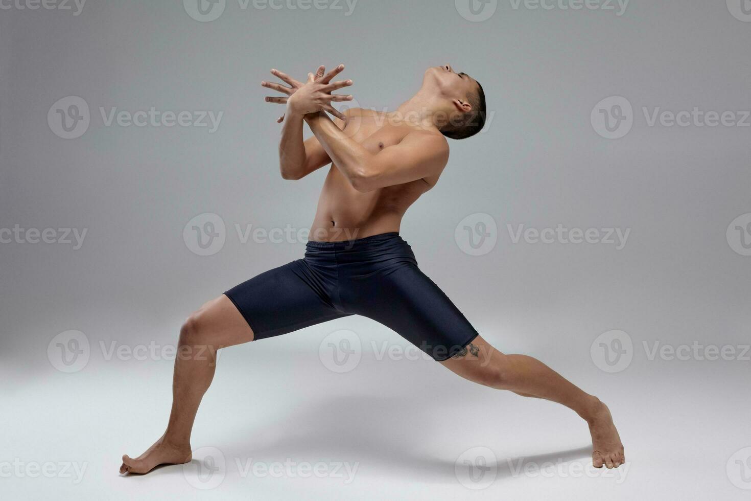 Photo of a handsome man ballet dancer, dressed in a black shorts, making a dance element against a gray background in studio.