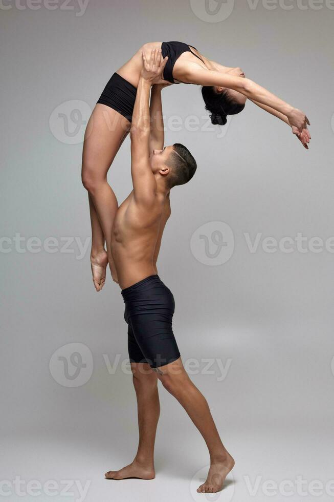 The couple of a young modern ballet dancers in black suits are posing over a gray studio background. photo