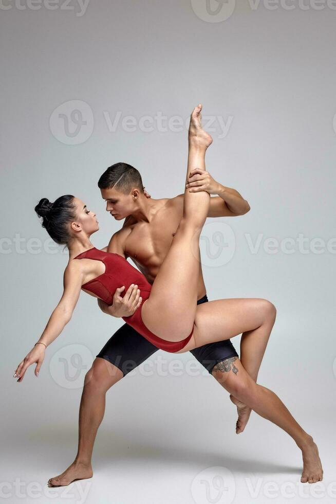 The couple of an athletic modern ballet dancers are posing against a gray studio background. photo