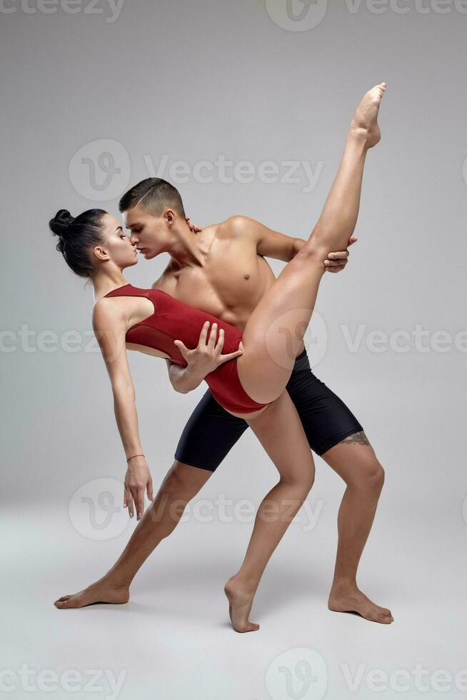 The couple of an athletic modern ballet dancers are posing against a gray studio background. photo