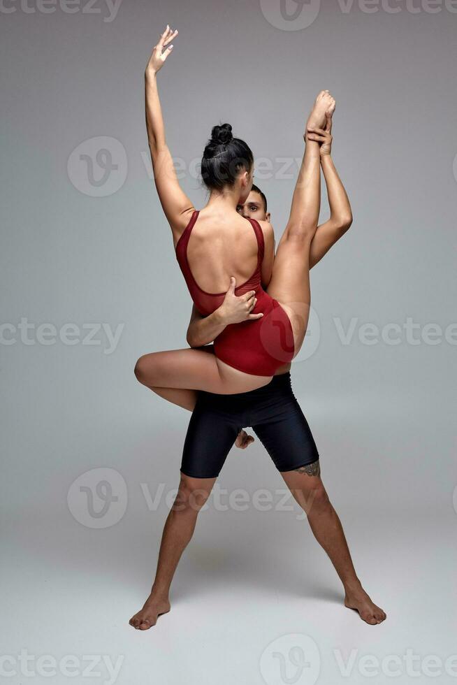 The couple of an athletic modern ballet dancers are posing against a gray studio background. photo