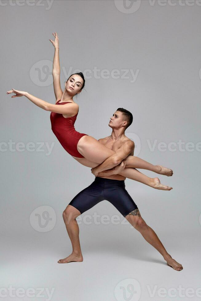 The couple of an athletic modern ballet dancers are posing against a gray studio background. photo