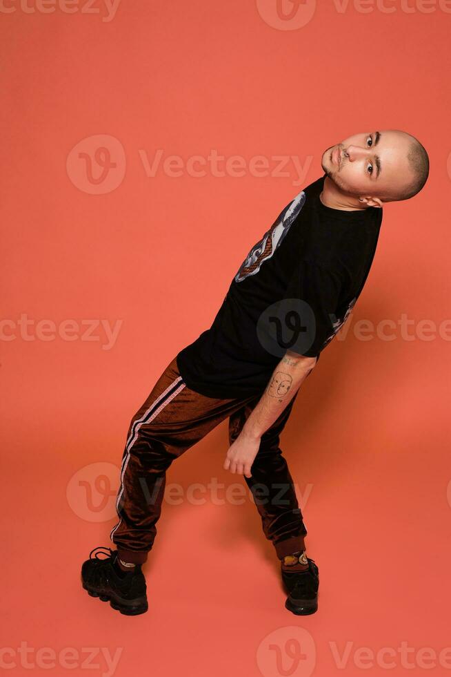 Studio shot of a young tattoed bald man posing against a pink background. 90s style. photo