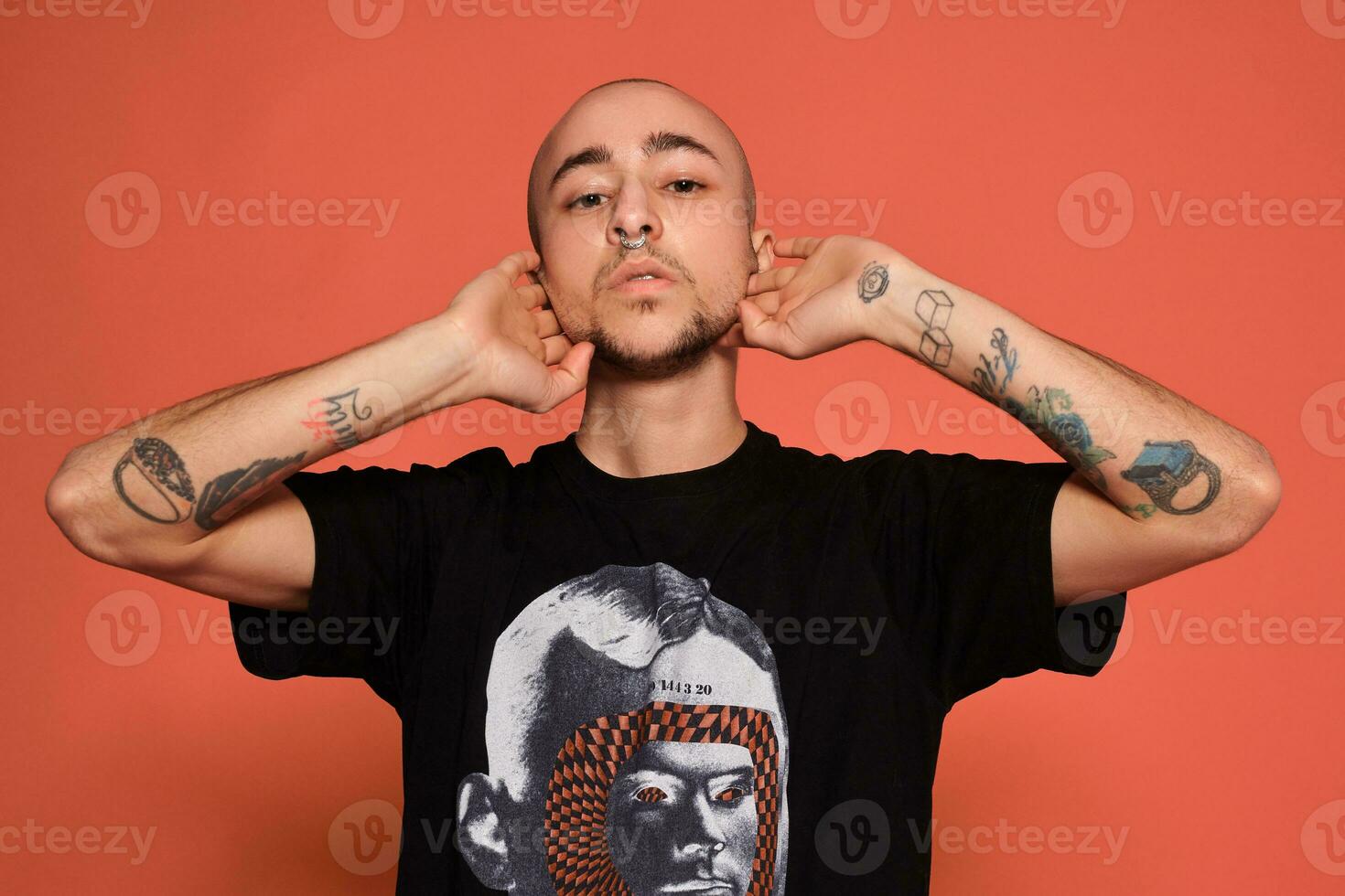 Studio shot of a young tattoed bald man posing against a pink background. 90s style. photo