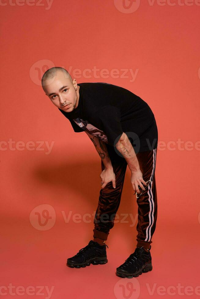 Studio shot of a young tattoed bald man posing against a pink background. 90s style. photo