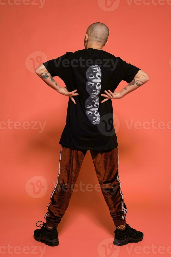 Studio shot of a young tattoed bald man posing against a pink background. 90s style. photo