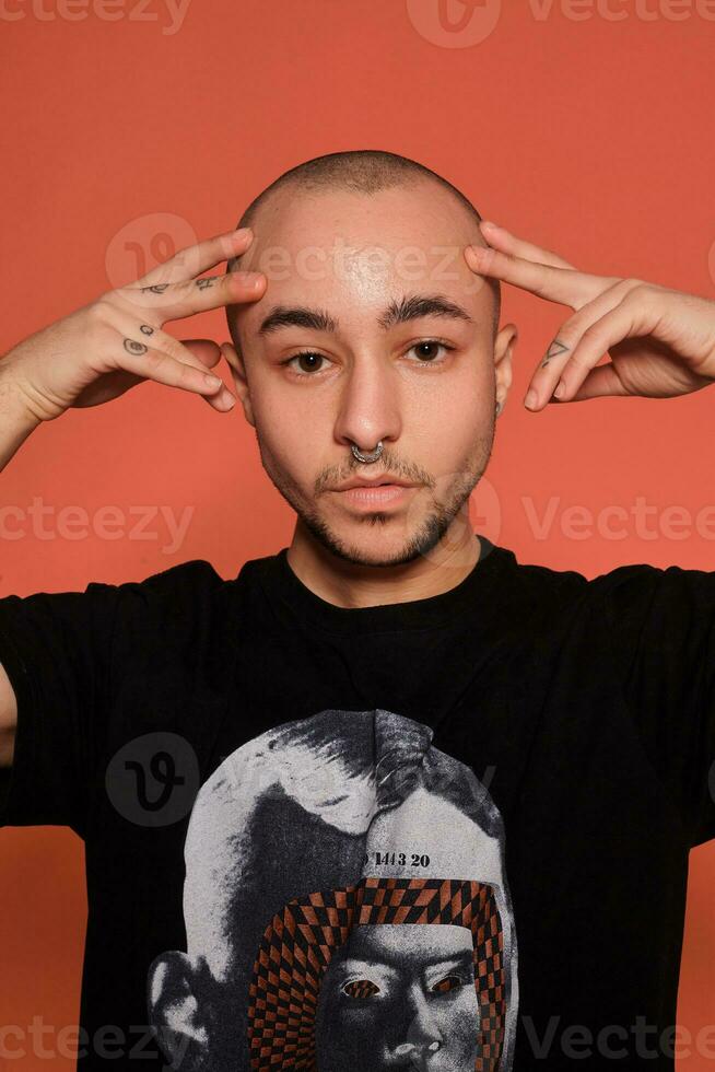 Studio shot of a young tattoed bald man posing against a pink background. 90s style. photo