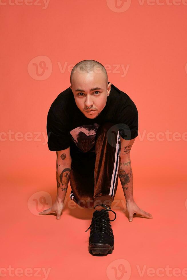 Studio shot of a young tattoed bald man posing against a pink background. 90s style. photo