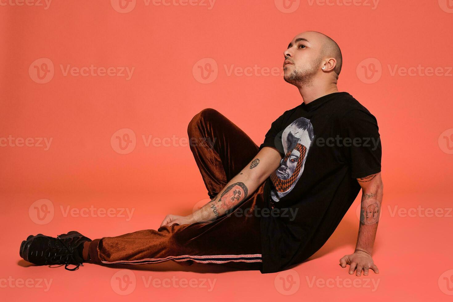 Studio shot of a young tattoed bald man posing against a pink background. 90s style. photo