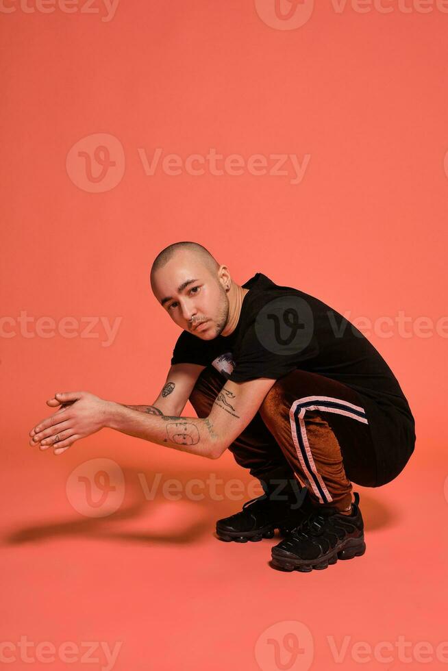 Studio shot of a young tattoed bald man posing against a pink background. 90s style. photo