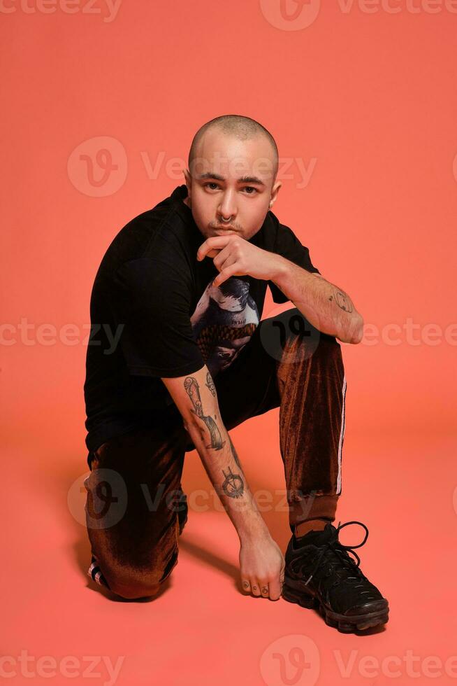 Studio shot of a young tattoed bald man posing against a pink background. 90s style. photo
