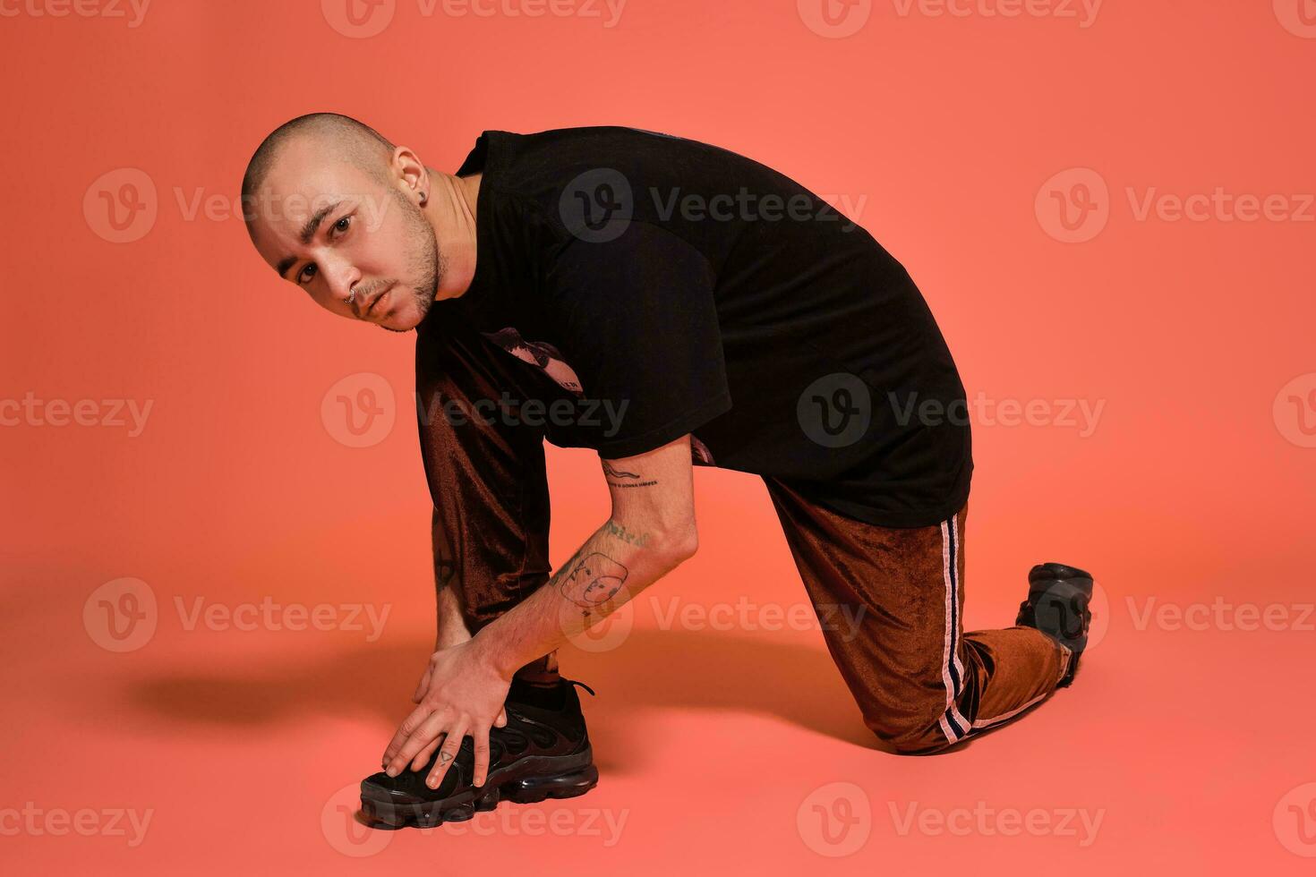 Studio shot of a young tattoed bald man posing against a pink background. 90s style. photo