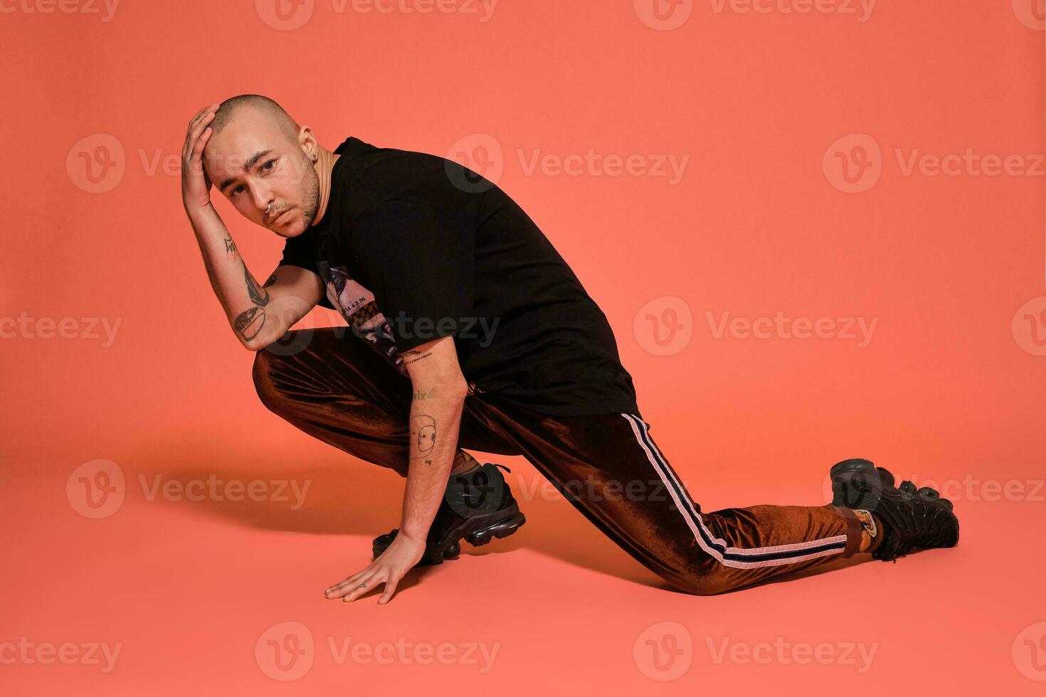 Studio shot of a young tattoed bald man posing against a pink background. 90s style. photo