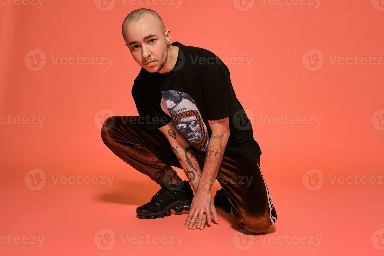 Studio shot of a young tattoed bald man posing against a pink background. 90s style. photo