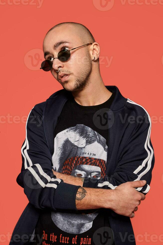 Studio shot of a young tattoed bald man posing against a pink background. 90s style. photo