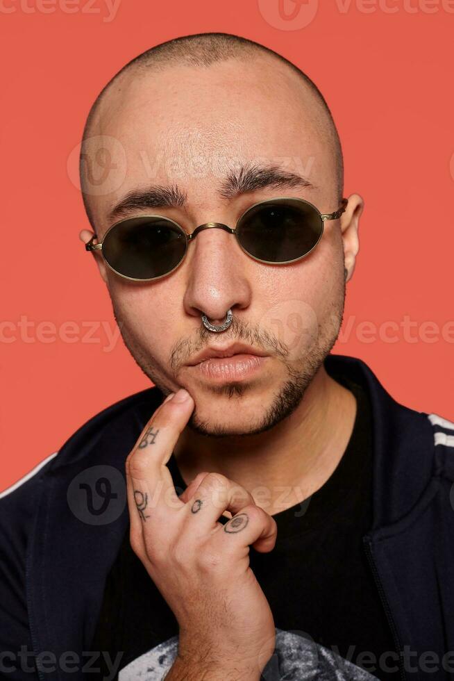 Studio shot of a young tattoed bald man posing against a pink background. 90s style. photo