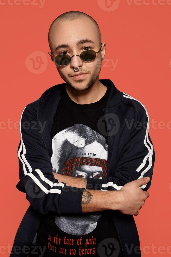 Studio shot of a young tattoed bald man posing against a pink background. 90s style. photo