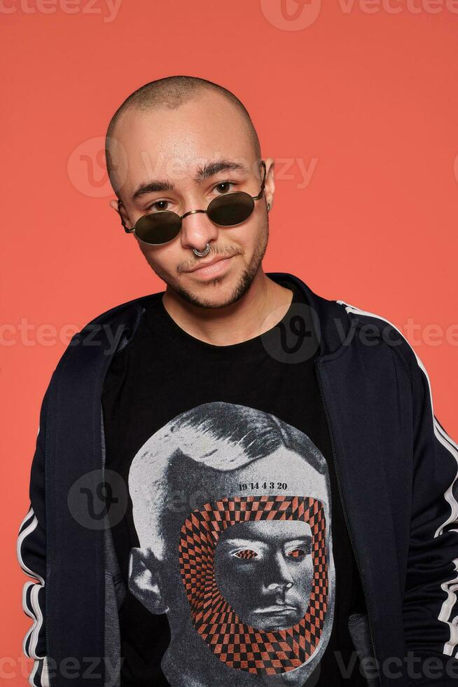 Studio shot of a young tattoed bald man posing against a pink background. 90s style. photo