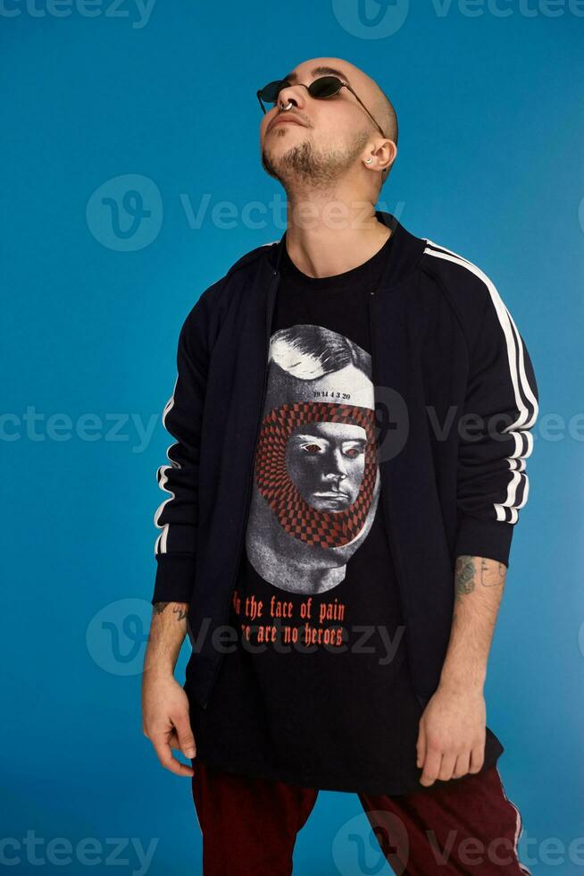 Studio shot of a young tattoed bald man posing against a blue background. 90s style. photo