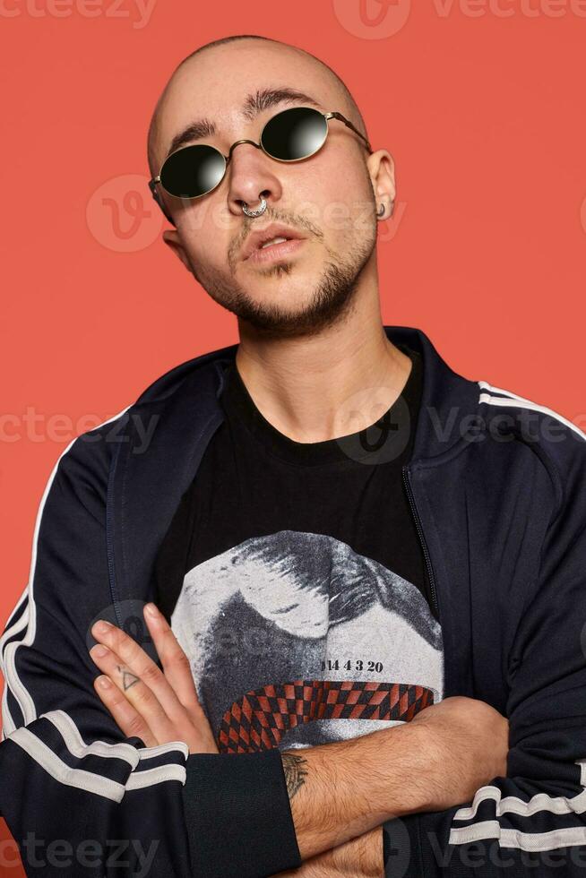 Studio shot of a young tattoed bald man posing against a pink background. 90s style. photo