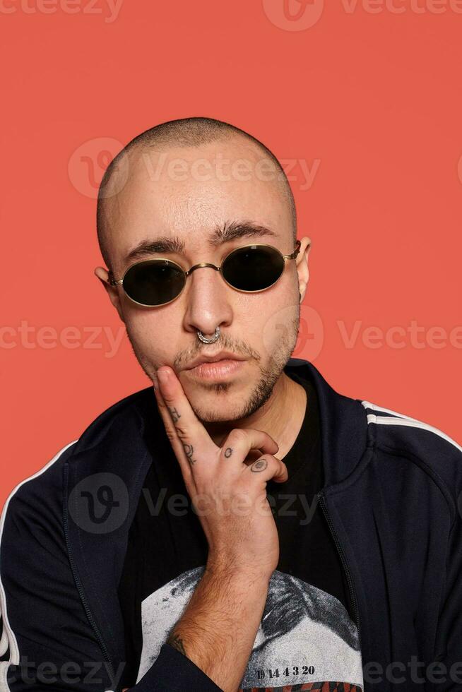 Studio shot of a young tattoed bald man posing against a pink background. 90s style. photo
