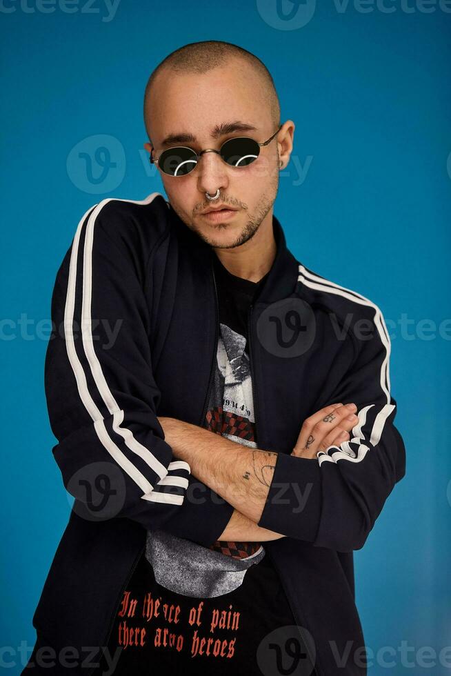 Studio shot of a young tattoed bald man posing against a blue background. 90s style. photo