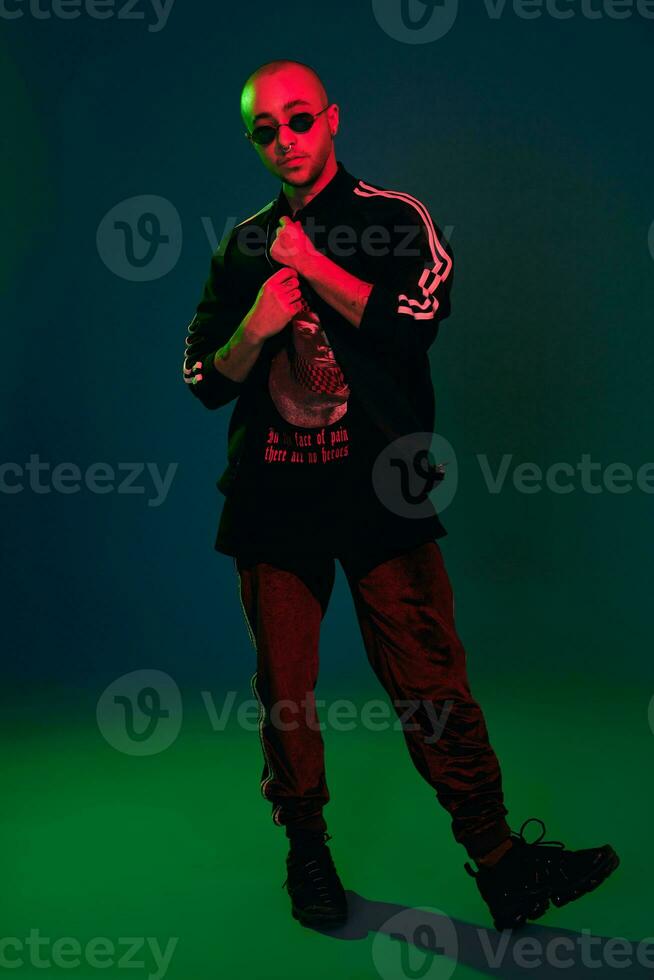 Studio shot of a young tattoed bald man posing against a colorful background. 90s style. photo