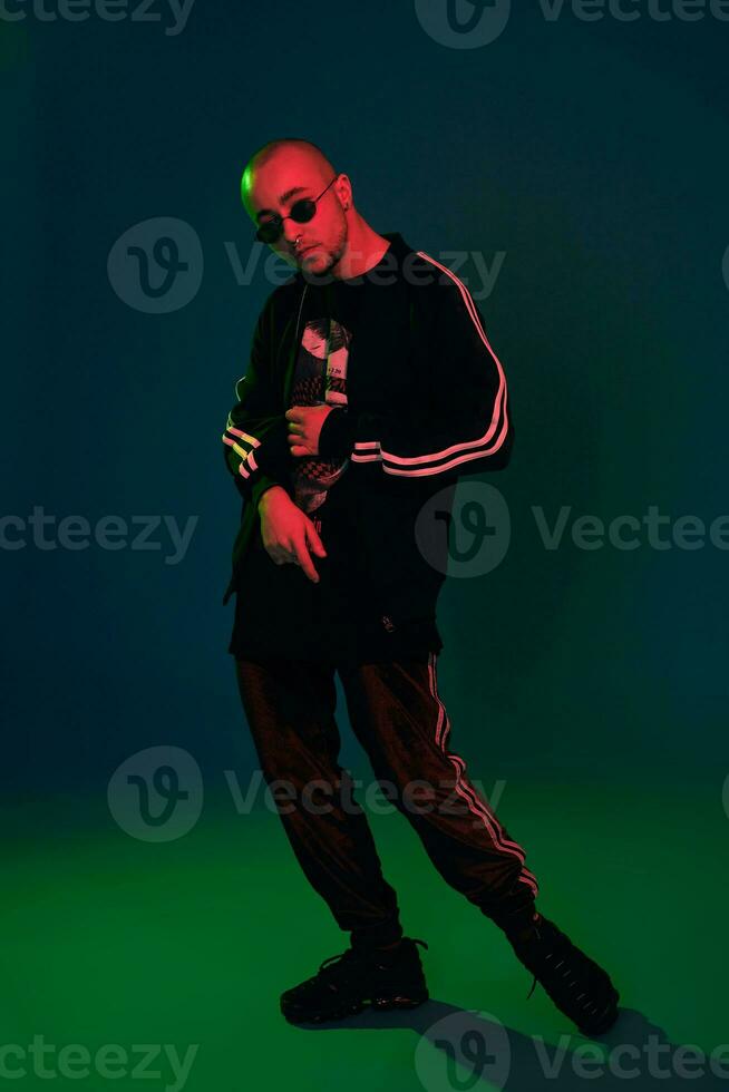 Studio shot of a young tattoed bald man posing against a colorful background. 90s style. photo