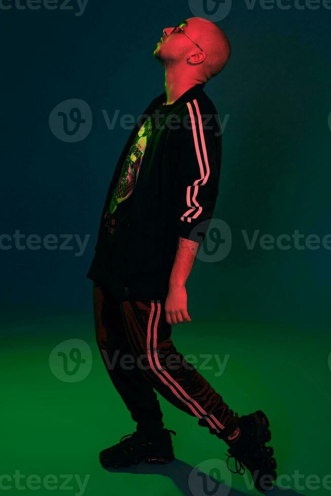 Studio shot of a young tattoed bald man posing against a colorful background. 90s style. photo