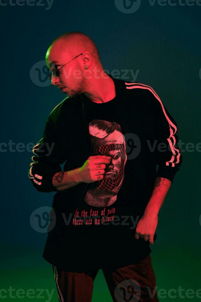 Studio shot of a young tattoed bald man posing against a colorful background. 90s style. photo