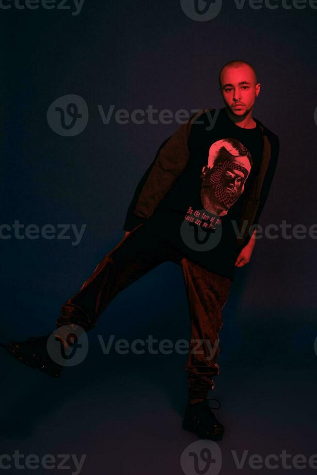 Studio shot of a young tattoed bald man posing against a dark blue background. 90s style. photo