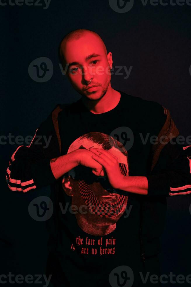 Studio shot of a young tattoed bald man posing against a dark blue background. 90s style. photo