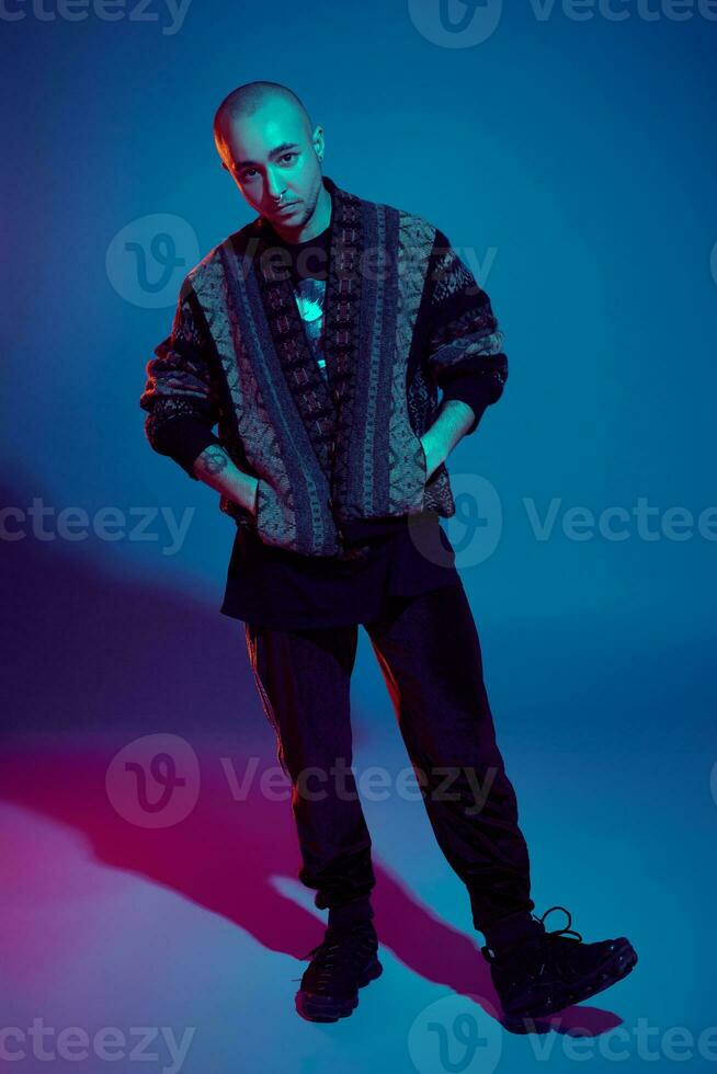 Studio shot of a young tattoed bald man posing against a colorful background. 90s style. photo