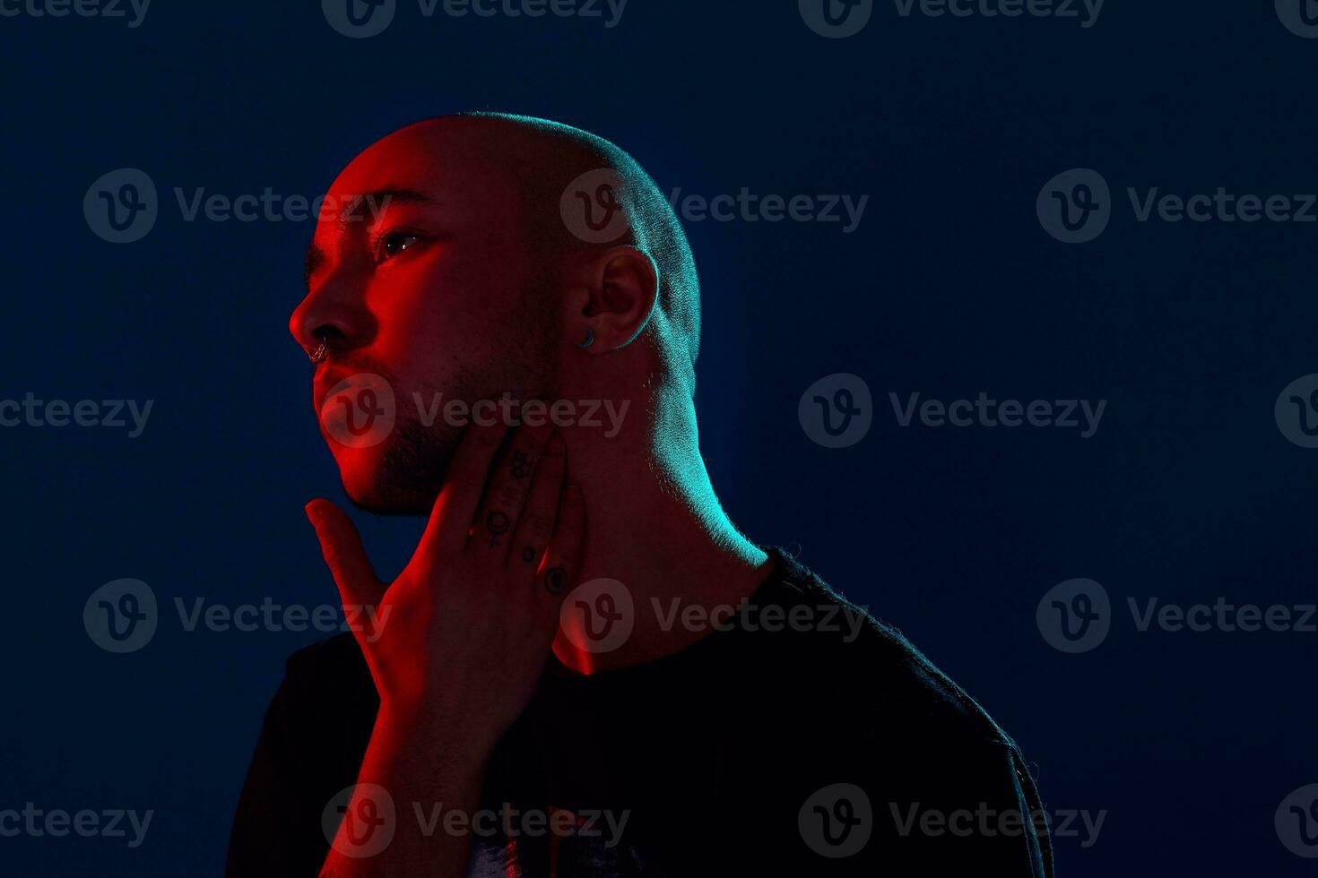 Studio shot of a young tattoed bald man posing against a blue background. 90s style. photo