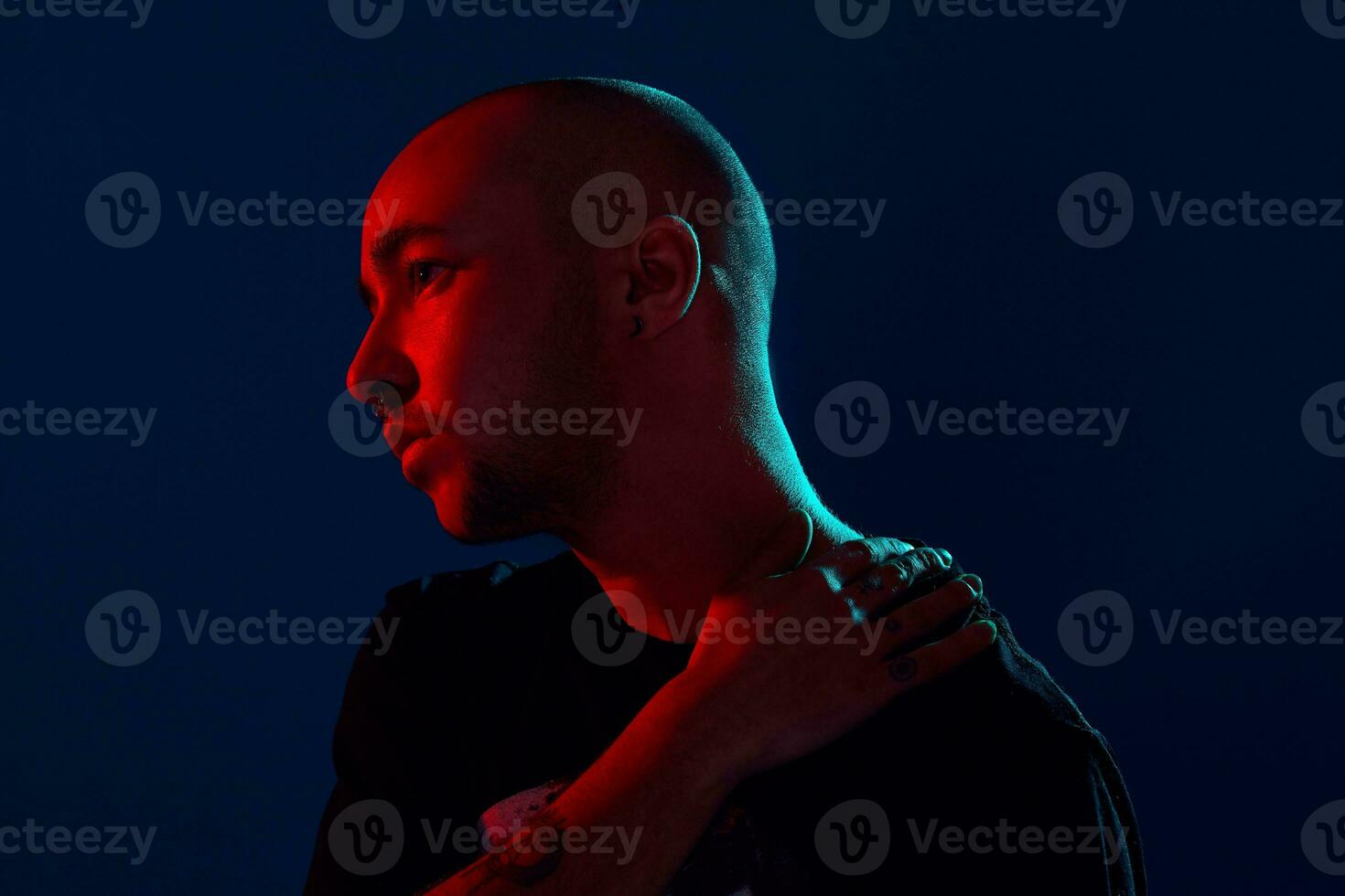 Studio shot of a young tattoed bald man posing against a blue background. 90s style. photo