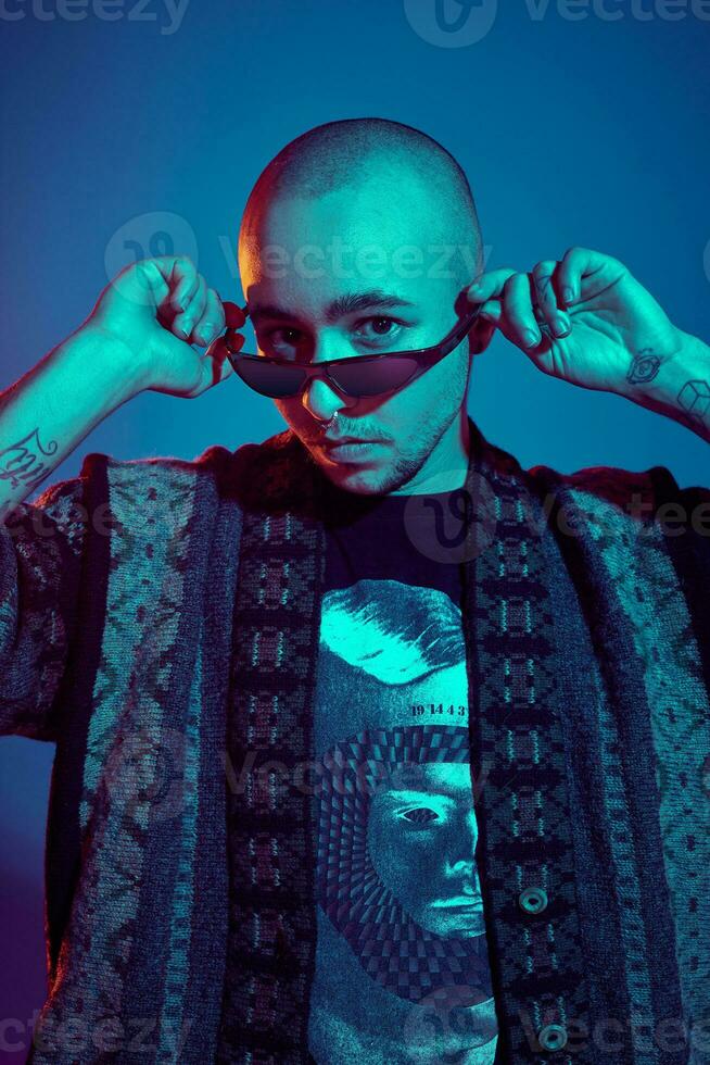 Studio shot of a young tattoed bald man posing against a blue background. 90s style. photo