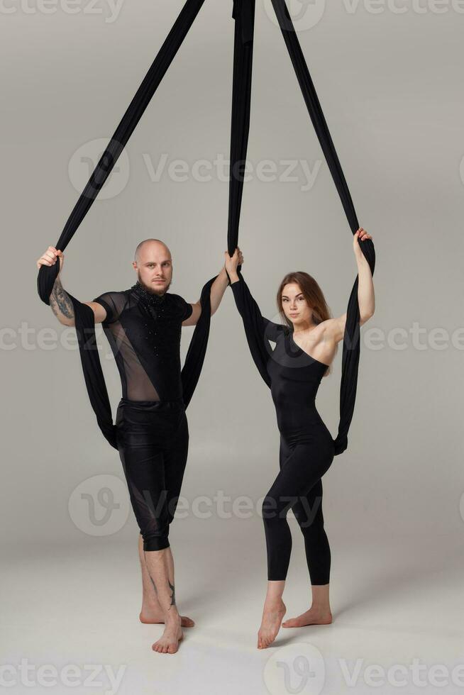 Beautiful girl and an athletic man in a black sport suits are performing an acrobatic elements in a studio. photo