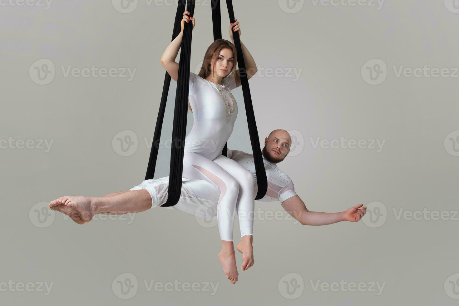 Beautiful girl and an athletic man in a white sport suits are performing an acrobatic elements in a studio. photo