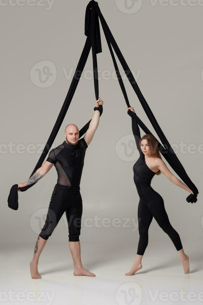 Beautiful girl and an athletic man in a black sport suits are performing an acrobatic elements in a studio. photo