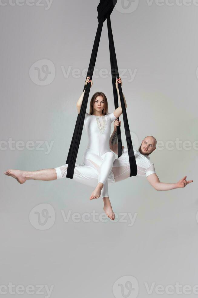 Beautiful girl and an athletic man in a white sport suits are performing an acrobatic elements in a studio. photo