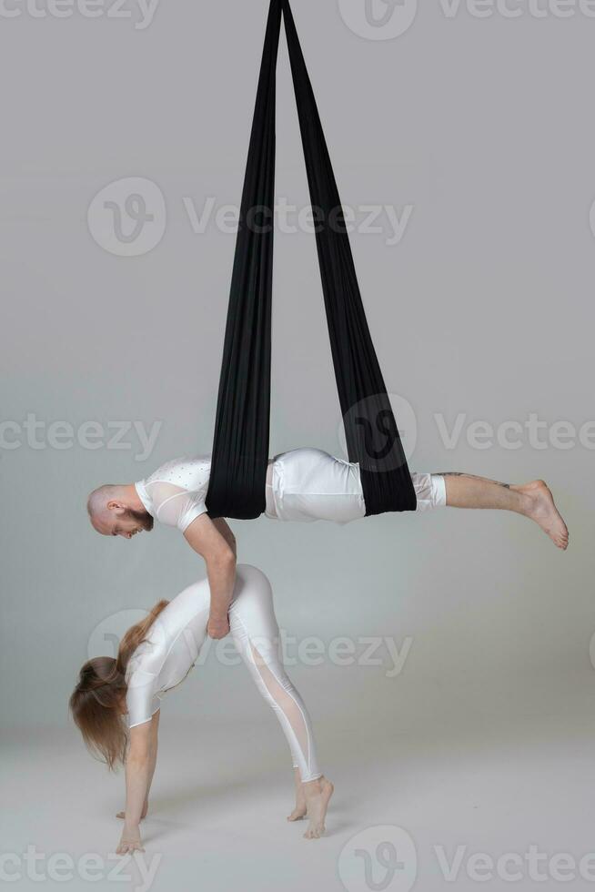 Beautiful girl and an athletic man in a white sport suits are performing an acrobatic elements in a studio. photo