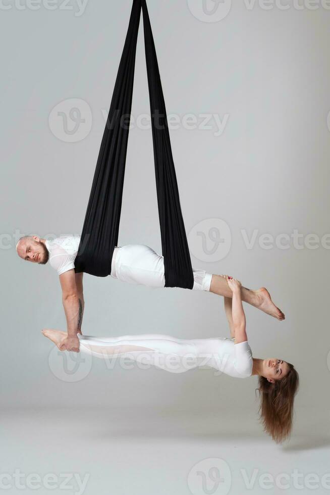 Beautiful girl and an athletic man in a white sport suits are performing an acrobatic elements in a studio. photo