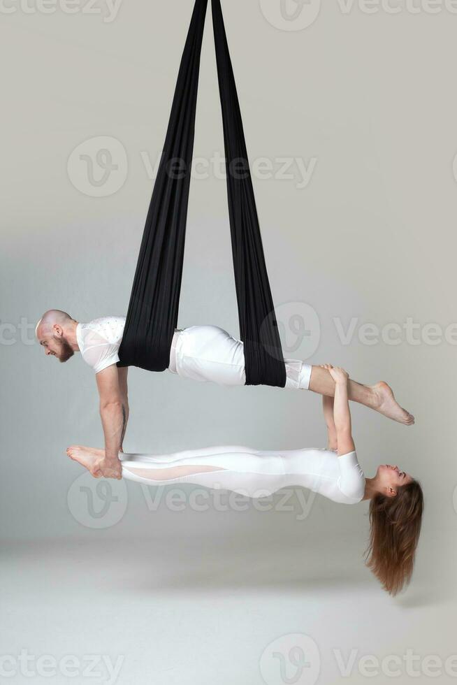 Beautiful girl and an athletic man in a white sport suits are performing an acrobatic elements in a studio. photo