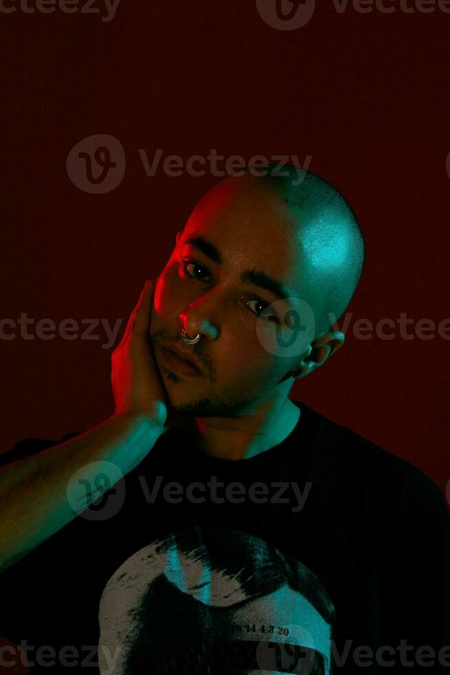 Studio shot of a young tattoed bald man posing against a red background. 90s style. photo